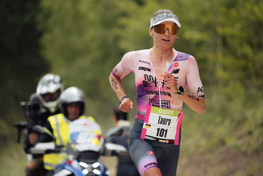 Athlete running in a triathlon with a blurred background of spectators and camera operators.